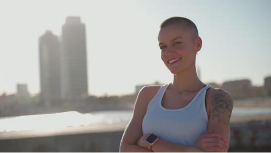 Woman with Roundry Head Wearing Fitness Tracker by the Waterfront, Highlighting Scalp Sun Protection While Maintaining a Shaved Head with Roundry