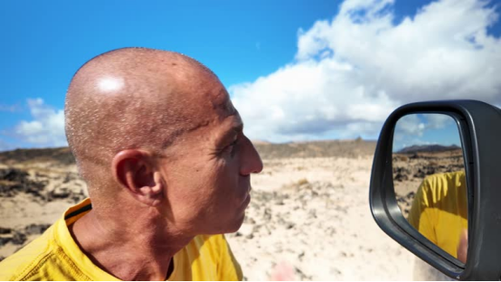 Bald head (groomed with a Roundry) on a man by a car in a desert landscape.