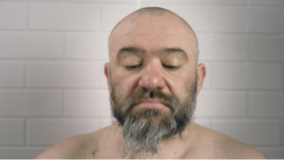 Man with a bald head (trimmed via a Roundry) and a gray beard, against a tiled wall.