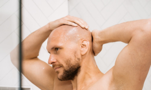 A man massaging his scalp in the shower, preparing for a clean, smooth shave with a head shaver.