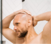 A man massaging his scalp in the shower, preparing for a clean, smooth shave with a head shaver.