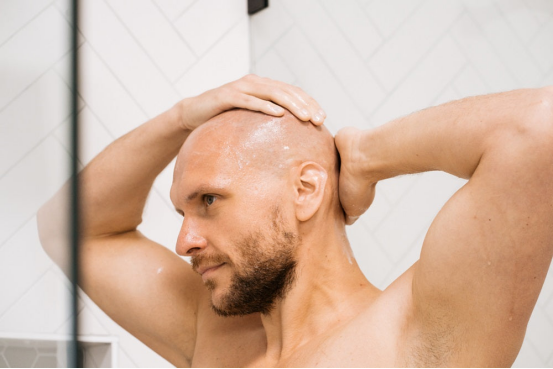 A man massaging his scalp in the shower, preparing for a clean, smooth shave with a head shaver.